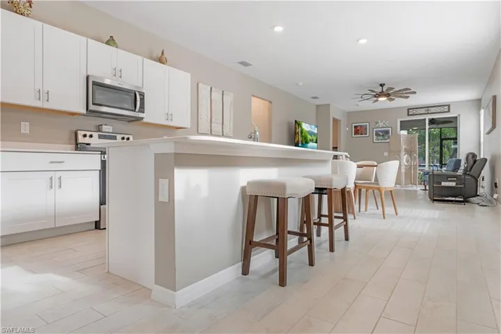 Kitchen with electric range, a kitchen breakfast bar, ceiling fan, and white cabinets
