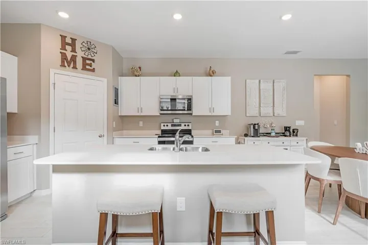 Kitchen featuring stainless steel appliances, an island with sink, white cabinets, sink, and a kitchen bar
