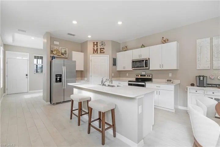 Kitchen featuring appliances with stainless steel finishes, white cabinets, a kitchen island with sink, a breakfast bar, and sink