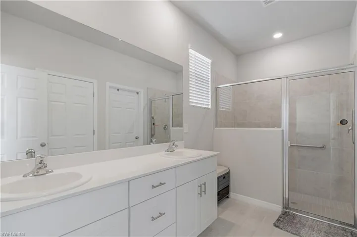 Bathroom featuring vanity with extensive cabinet space, an enclosed shower, double sink, and tile flooring