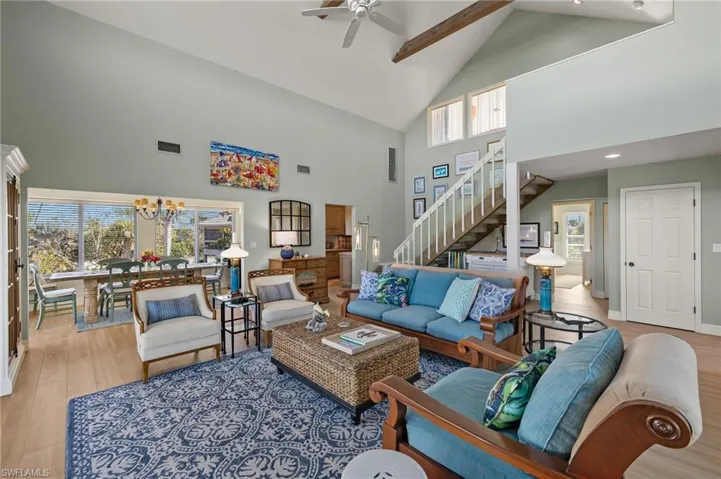 Living room with high vaulted ceiling, wood finished floors, stairs, a ceiling fan, and a chandelier