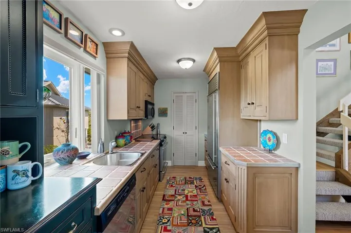 Kitchen with light wood-style floors, stainless steel appliances, tile counters, and light brown cabinets