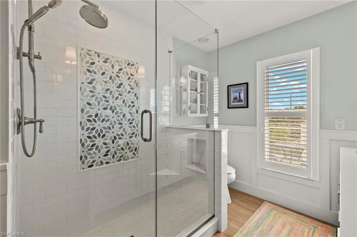Full bath featuring light wood-style flooring, a shower stall, a wainscoted wall, and a decorative wall