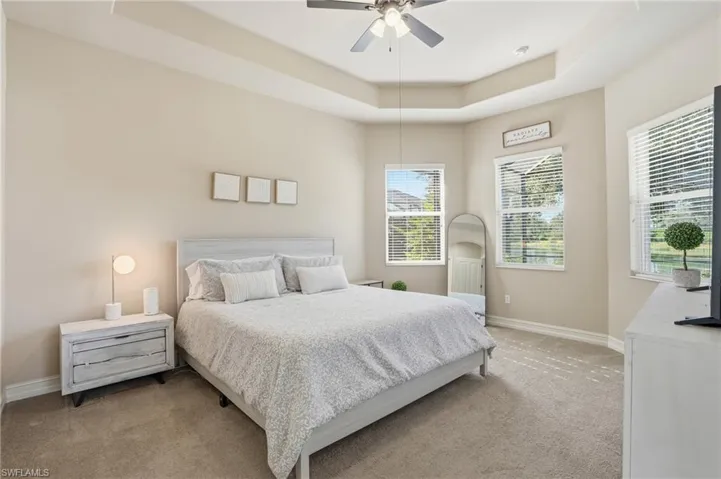 Carpeted bedroom featuring a raised ceiling and a ceiling fan