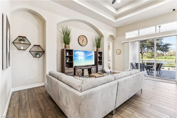 Living room featuring wood finished floors, a tray ceiling, arched walkways, and a towering ceiling