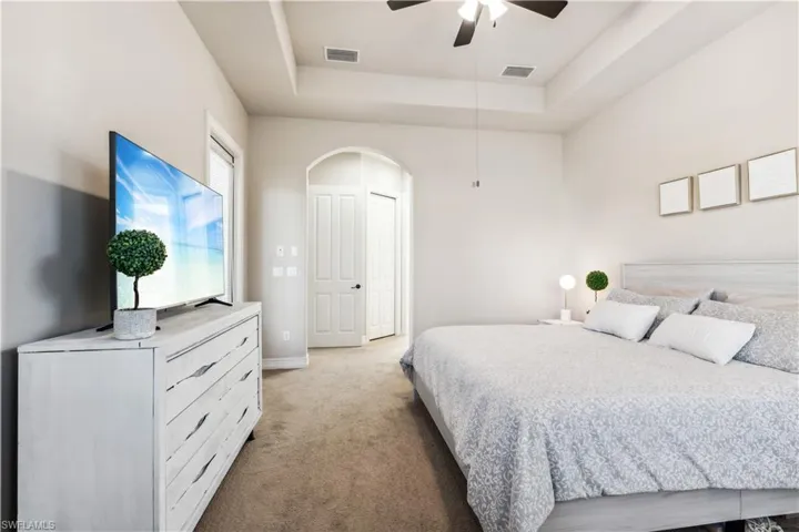 Carpeted bedroom with a tray ceiling and a ceiling fan