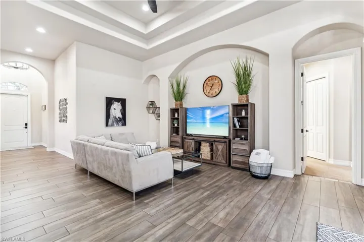 Living area with arched walkways, light wood finished floors, a raised ceiling, and recessed lighting