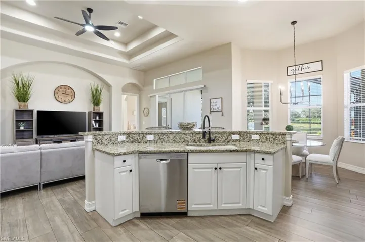 Kitchen featuring white cabinetry, open floor plan, light stone counters, stainless steel dishwasher, and a kitchen island with sink