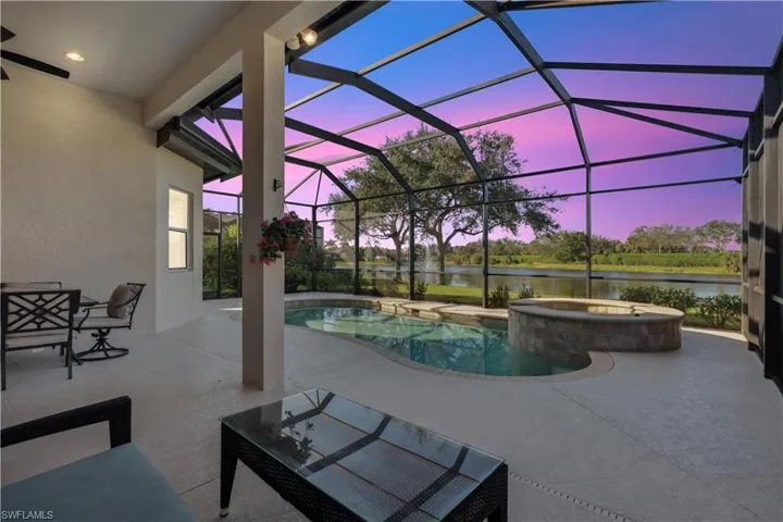 Pool at dusk with a sunroom, a patio, a lanai, a pool with connected hot tub, and a water view