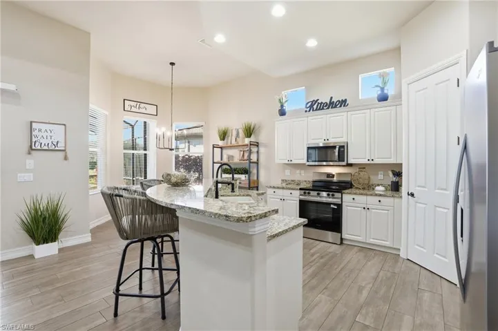 Kitchen with a kitchen island with sink, white cabinetry, appliances with stainless steel finishes, hanging light fixtures, and a chandelier