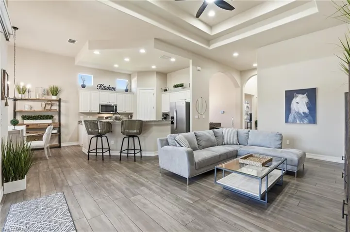 Living area with a raised ceiling, arched walkways, ceiling fan, wood tiled floors, and recessed lighting