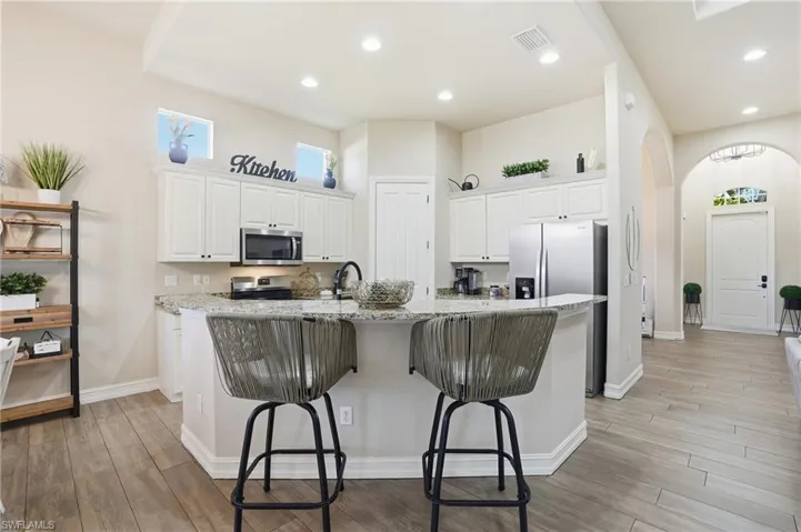Kitchen with light stone counters, white cabinetry, a kitchen breakfast bar, a kitchen island with sink, and light wood finished floors