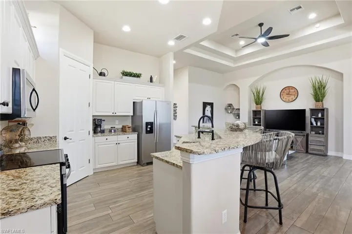 Kitchen featuring an island with sink, stainless steel appliances, white cabinetry, recessed lighting, and a breakfast bar area
