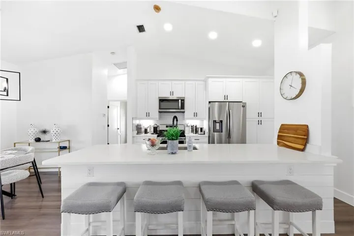 Kitchen featuring dark wood-type flooring, a breakfast bar area, white cabinetry, stainless steel appliances, and lofted ceiling