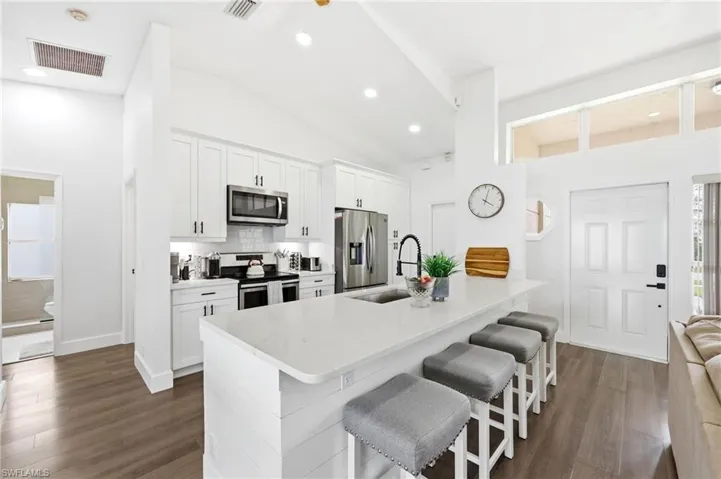 Kitchen with white cabinets, stainless steel appliances, a kitchen bar, dark wood-style flooring, and vaulted ceiling