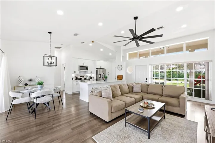 Living area with dark wood-style floors, ceiling fan, suspended lighting, and lofted ceiling