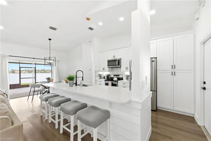 Kitchen with white cabinets, stainless steel appliances, a breakfast bar area, lofted ceiling, and light stone counters