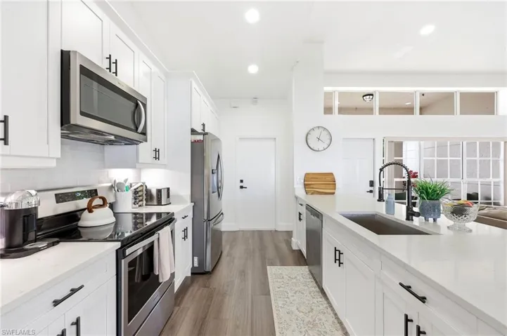 Kitchen featuring stainless steel appliances, white cabinets, light stone counters, and recessed lighting