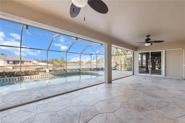 View of swimming pool with glass enclosure, ceiling fan, a patio area, and a water view