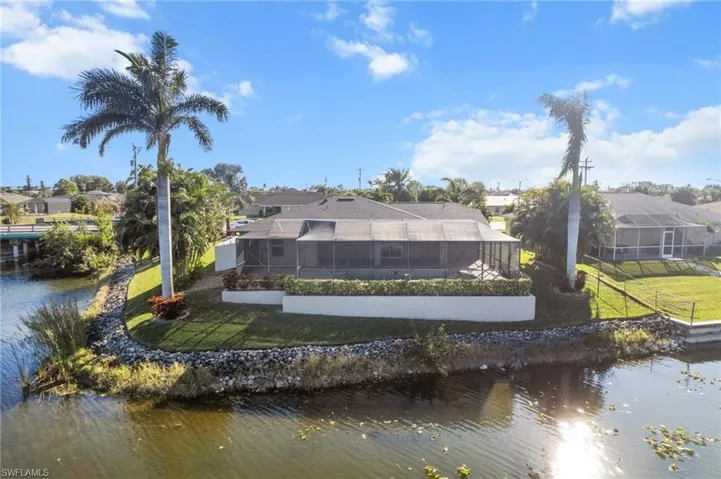 Rear view of property featuring a water view, glass enclosure, and a lawn