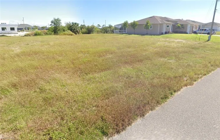 The property features an expansive, undeveloped lot with a visible paved road along one edge
