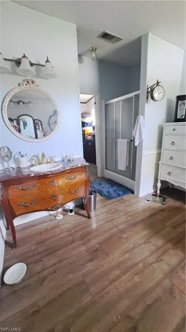 Bathroom with a textured ceiling, wood finished floors, a shower stall, and vanity