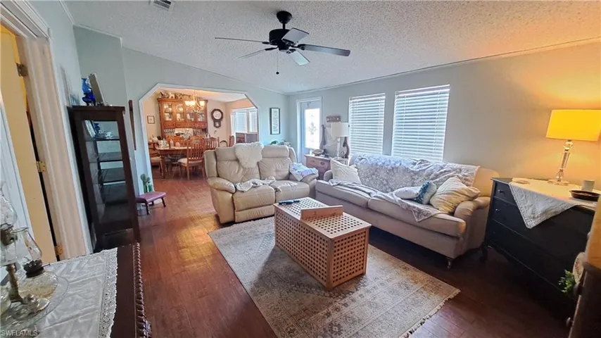 Living room with arched walkways, wood-type flooring, vaulted ceiling, a textured ceiling, and a ceiling fan