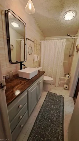 Full bathroom with a textured ceiling, vanity, shower / bath combo, and vaulted ceiling