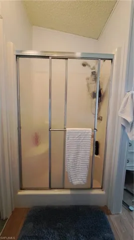 Bathroom with a textured ceiling, lofted ceiling, a shower stall, and wood finished floors