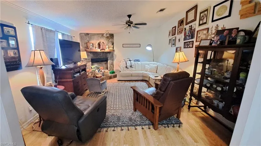 Living room featuring ceiling fan, wood finished floors, a fireplace, and a textured ceiling