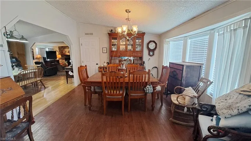 Dining space with arched walkways, a chandelier, wood finished floors, a textured ceiling, and crown molding