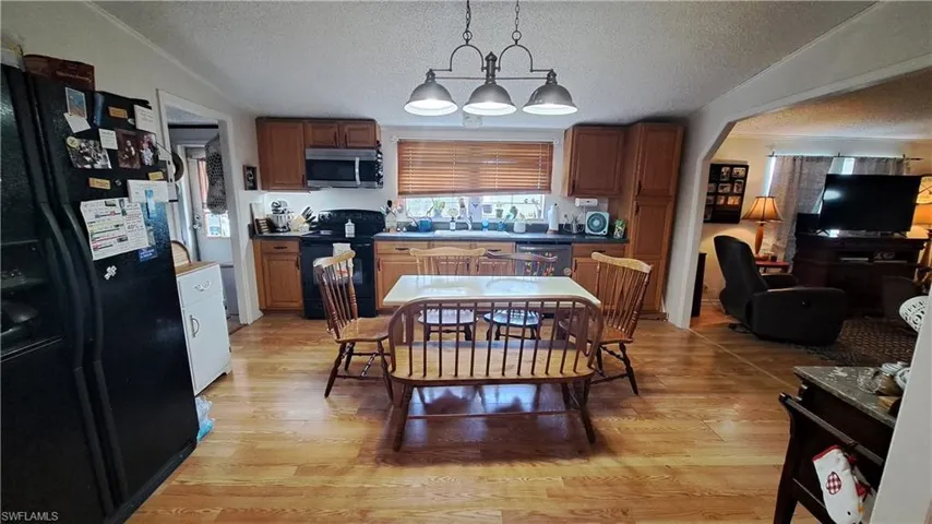 Kitchen featuring black appliances, a textured ceiling, light wood-style flooring, dark countertops, and pendant lighting