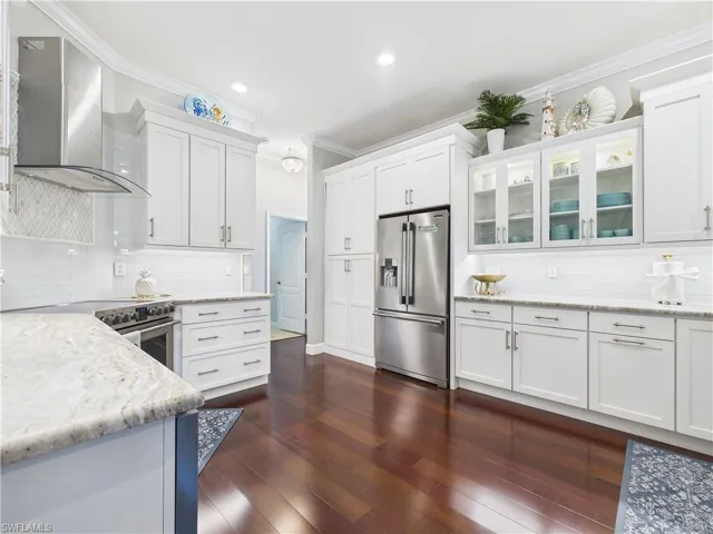 Kitchen with decorative backsplash, wall chimney exhaust hood, appliances with stainless steel finishes, white cabinets, and ornamental molding