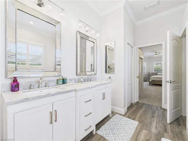 Ensuite bathroom with crown molding, double vanity, ceiling fan, and dark wood-style floors