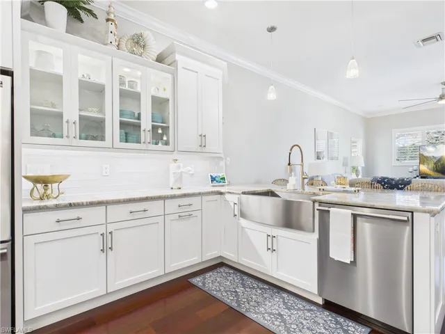 Kitchen with white cabinets, stainless steel dishwasher, light stone countertops, and ornamental molding
