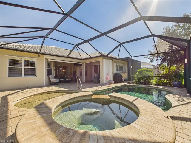 View of pool with glass enclosure, a pool with connected hot tub, a sunroom, a patio area, and grilling area