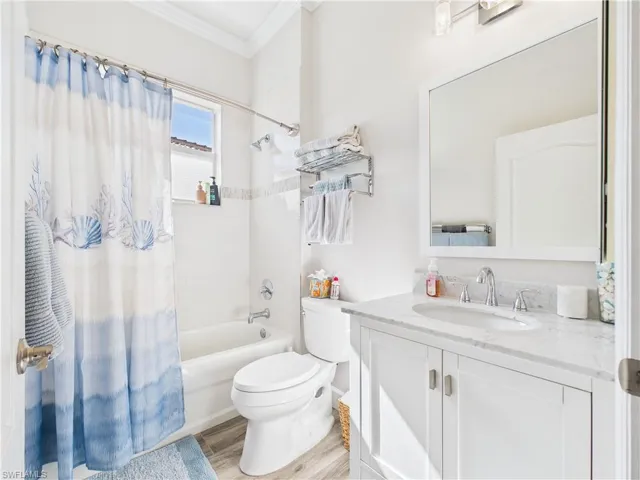 Full bath with vanity, shower / bath combination with curtain, ornamental molding, and light wood-type flooring