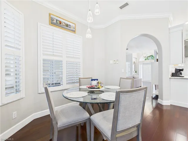 Dining room with arched walkways, dark wood-style floors, and ornamental molding