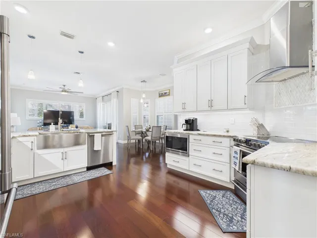 Kitchen with ornamental molding, white cabinets, wall chimney range hood, stainless steel appliances, and a peninsula