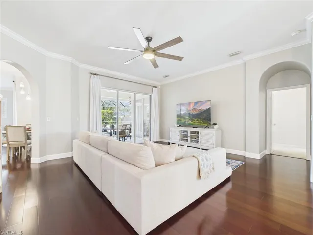 Living room with arched walkways, ornamental molding, dark wood-type flooring, and ceiling fan