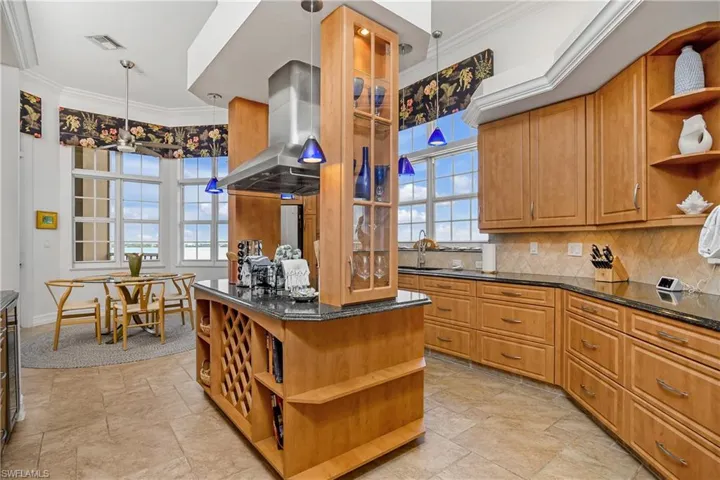Kitchen featuring island exhaust hood, pendant lighting, tasteful backsplash, and plenty of natural light
