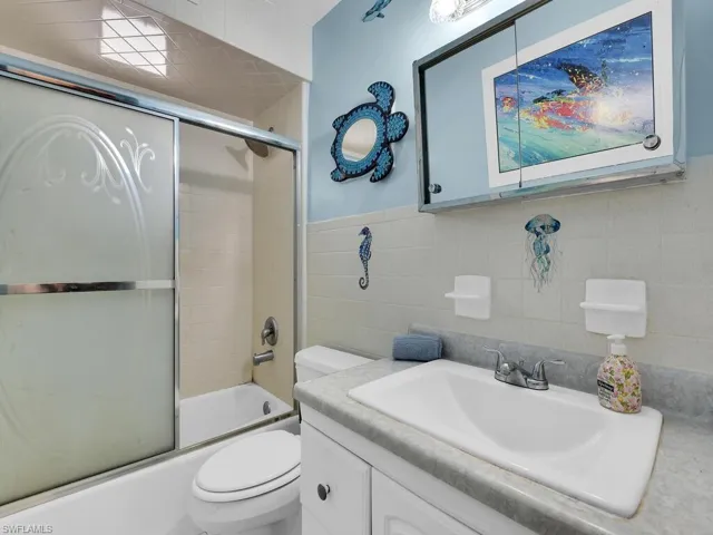 Full bathroom featuring toilet, tile walls, vanity, and shower / bath combination with glass door