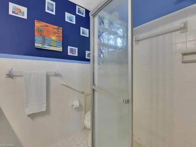 Bathroom with toilet, walk in shower, tile walls, and tile patterned flooring