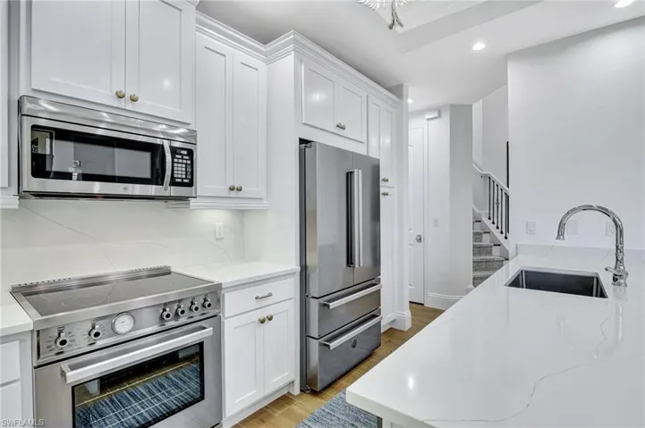 Kitchen with sink, premium Italian appliances, quartz counters and backsplash, snack bar, and white cabinets with pantry