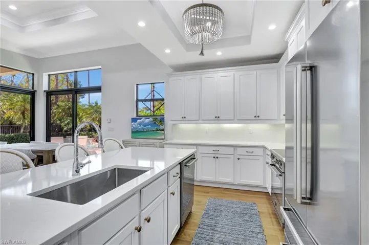 Kitchen featuring quartz countertops and backsplash, stainless steel italian appliances, a tray ceiling, new sink, snack bar, white cabinetry and pantry