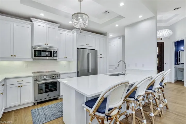 Kitchen with white cabinetry, new sink, snack bar, premium Italian appliances, a raised ceiling, and pendant lighting