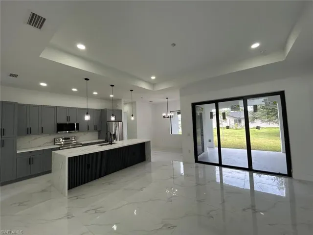 Kitchen featuring light tile patterned flooring, stainless steel appliances, an island with sink, and a tray ceiling