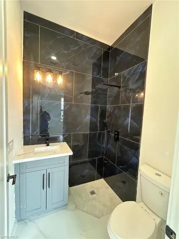 Bathroom featuring vanity, tile patterned floors, tile walls, a tile shower, and toilet