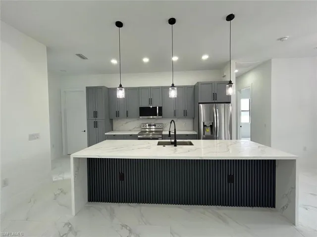 Kitchen with light tile patterned floors, light stone counters, stainless steel appliances, a spacious island, and sink