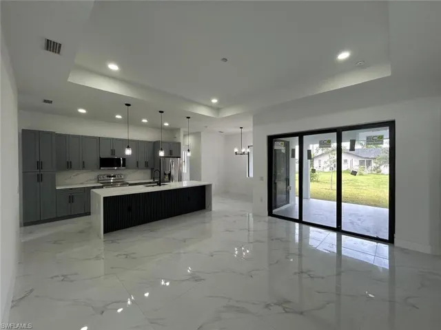 Kitchen with light tile patterned flooring, an island with sink, appliances with stainless steel finishes, and a tray ceiling